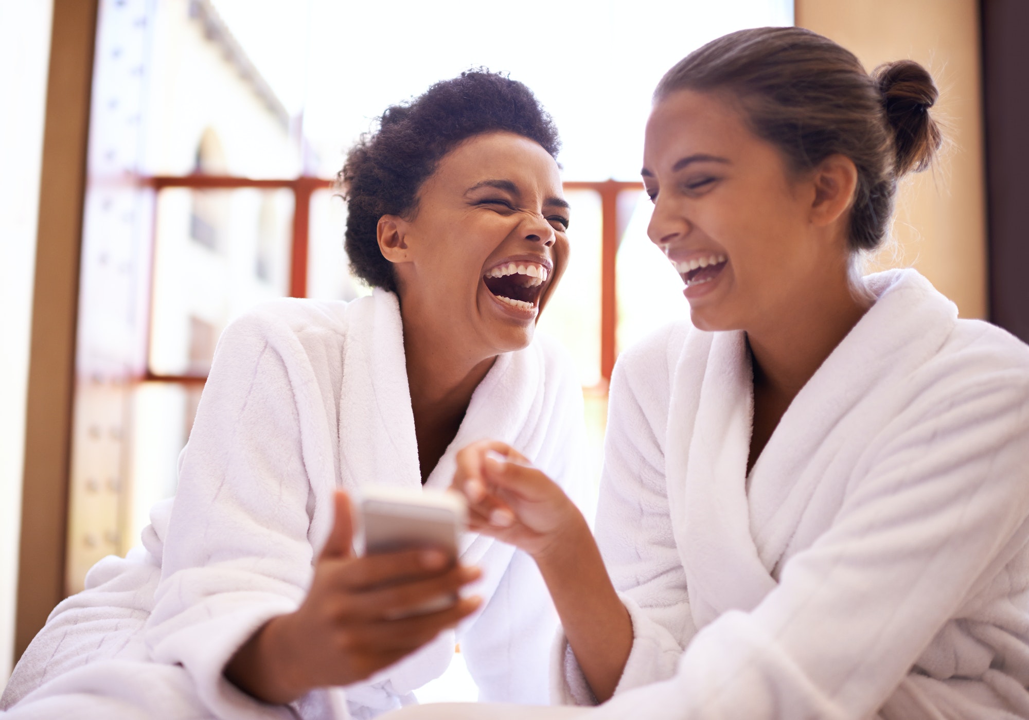Girls day at the spa. Shot of two friends in bathrobes using a cellphone at a spa.